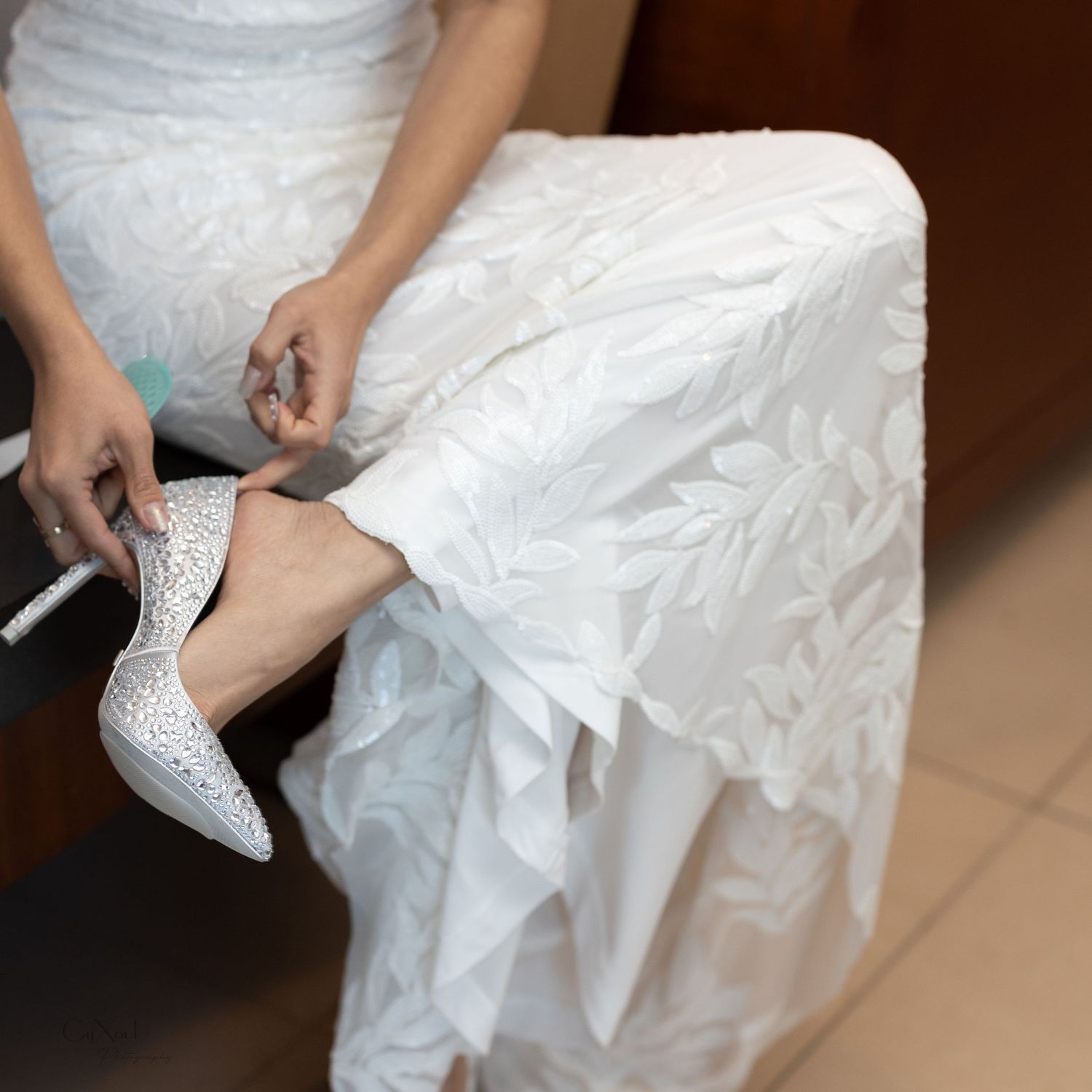 Close-up of a bride putting on sparkly white wedding heels while sitting.