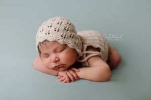 Sleeping baby wearing delicate lace bonnet on soft mint green background.