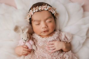 Sleeping newborn in pink lace dress with floral crown on soft pink blanket.