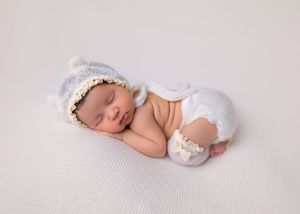 A sleeping newborn in a white knit bonnet lying on a textured cream colored blanket.