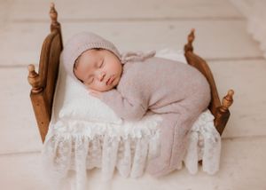 Baby napping on wooden bed with ruffled bedding wearing soft pink knit outfit.