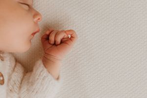 Close-up of sleeping baby's face and tiny hand in soft white knitwear.