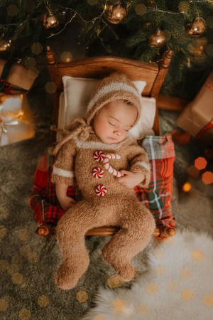 Sleeping baby wearing knit onesie with candy cane details surrounded by Christmas lights.
