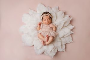 Sleeping newborn in pink outfit posed on white floral backdrop.