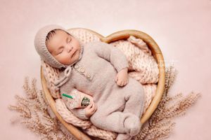 A sleeping infant in soft gray knitwear resting in a round basket with dried flowers.
