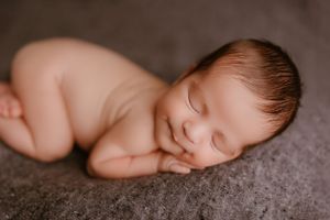 Peaceful sleeping newborn laying on side against grey textured background.