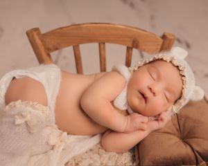 Peaceful baby napping on wooden chair wearing vintage lace bonnet and wrap.