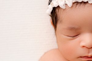 Peaceful sleeping baby with delicate white flower crown against soft pink background.