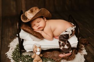 Sleeping newborn with cowboy hat and boots in rustic country-themed setup.