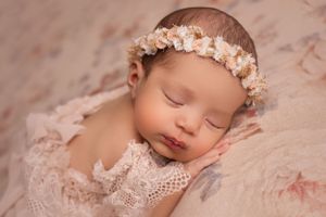 Sleeping newborn with floral headband lying on delicate pink lace fabric.