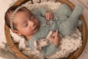 Peaceful sleeping infant in crown wearing soft grey knit outfit in wooden basket.