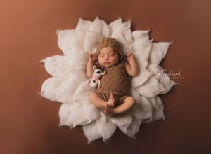 Sleeping infant cradled in white flower-shaped backdrop with brown knit outfit.