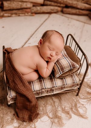 A peaceful sleeping infant on plaid pillows in a small metal bed with brown fabric.