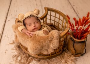 Sweet newborn sleeping in round woven basket with red flower decoration.