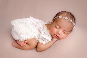 Sleeping baby in delicate white lace outfit against soft pink background.