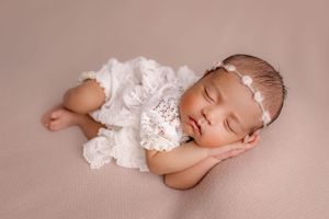 Peaceful sleeping infant wearing white lace outfit on pink background.