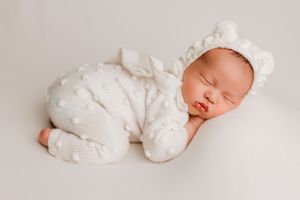 Peaceful sleeping infant in white lace outfit against simple white background.