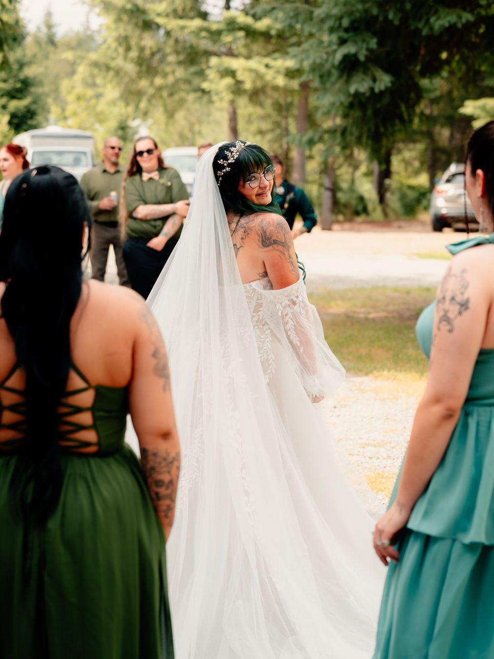 A bride in a lace wedding dress shows off her tattoos during an outdoor forest ceremony.