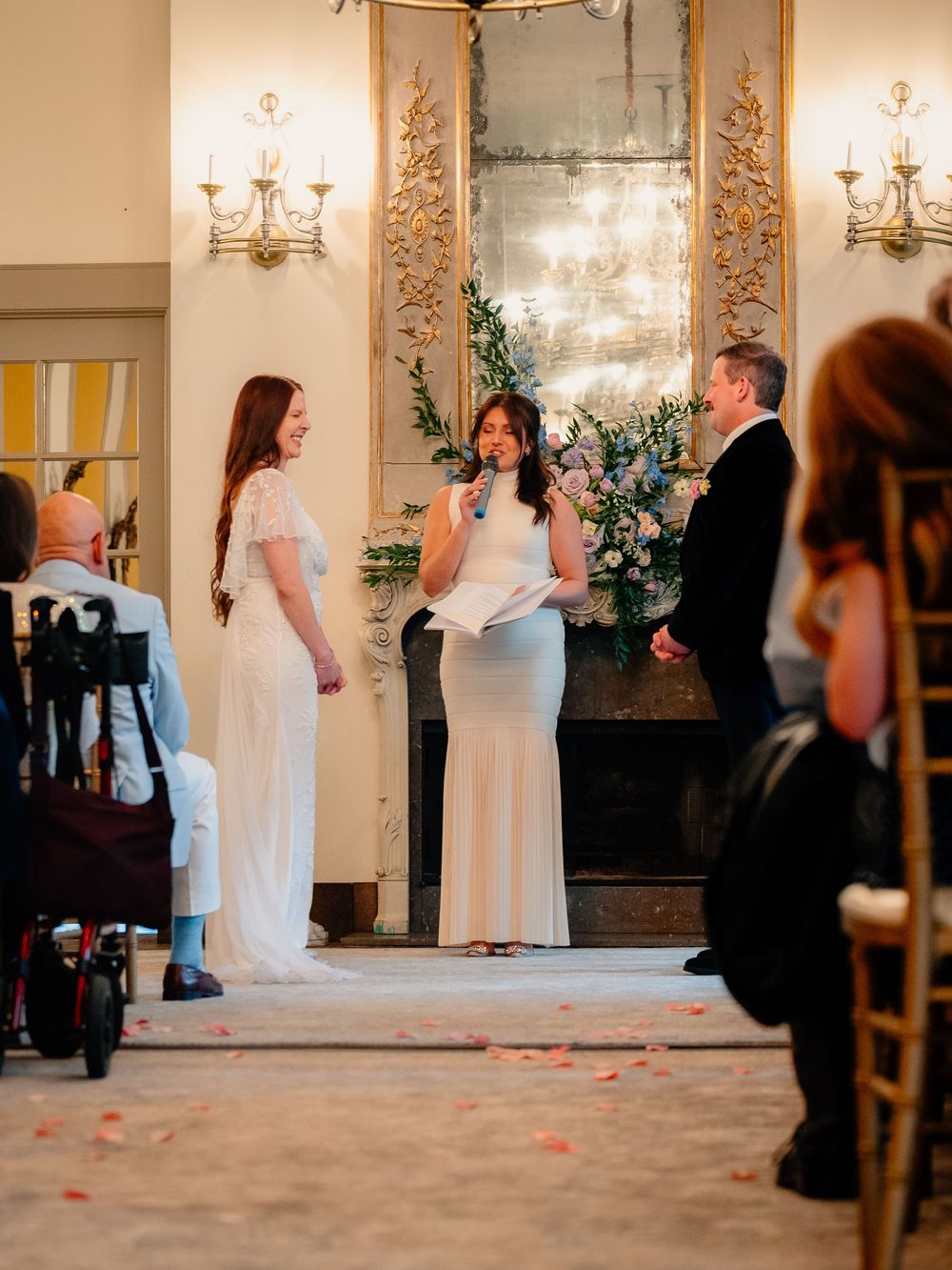 Wedding ceremony setup in an elegant ballroom with ornate mirrors and chandeliers.