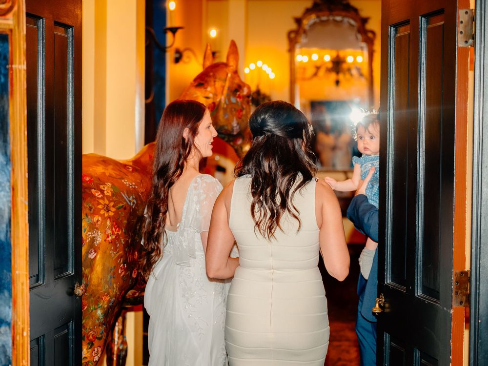 Two people in elegant white dresses share a moment at an evening wedding reception.