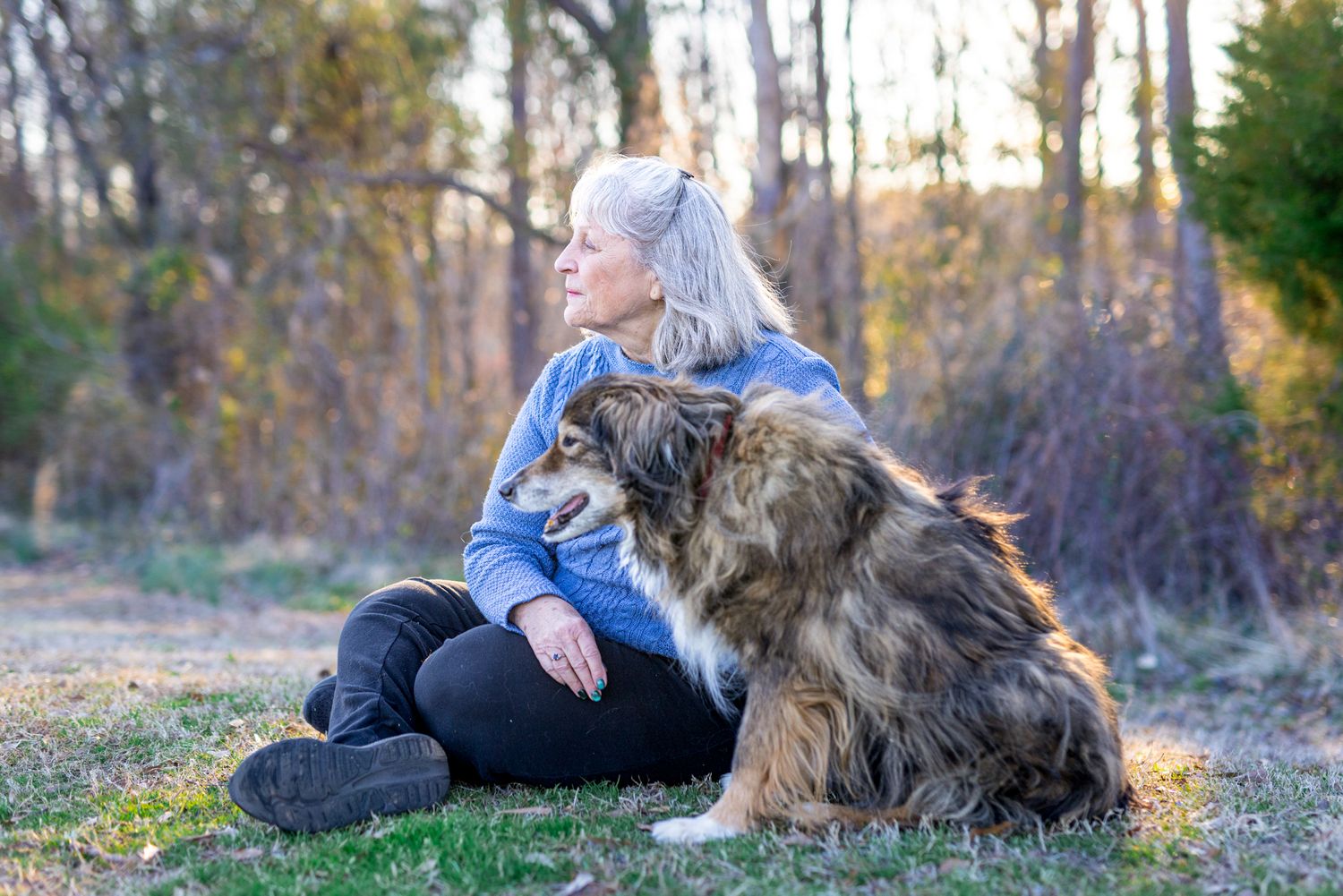 Tearful end-of-life pet photo session of a woman kissing her dog’s head outdoors in soft evening light.