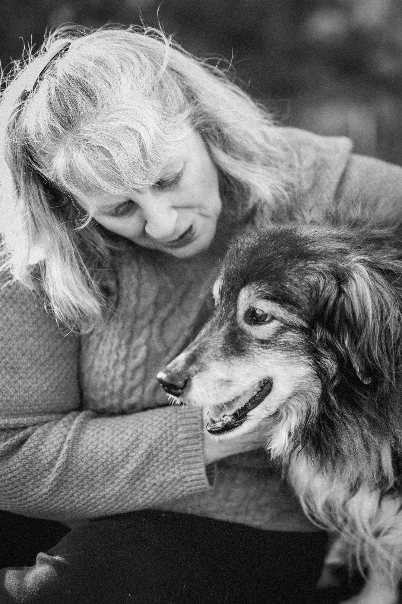 A peaceful farewell moment of a woman sitting beside her dog in the grass during their final photo session, Windsor Ontario.