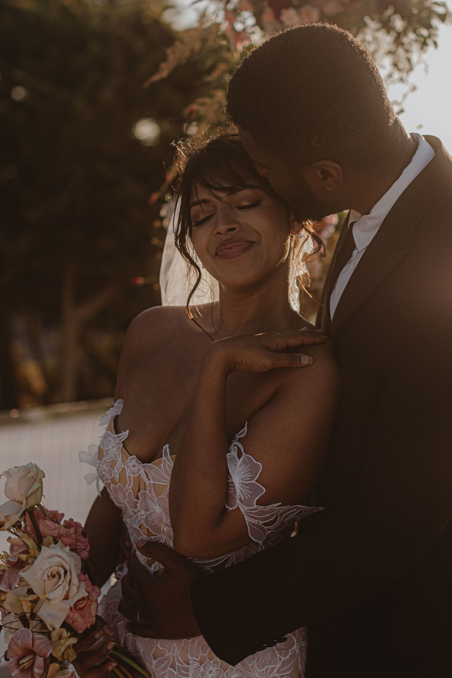 Romantic sunset wedding portrait with soft golden lighting and elegant white lace details.