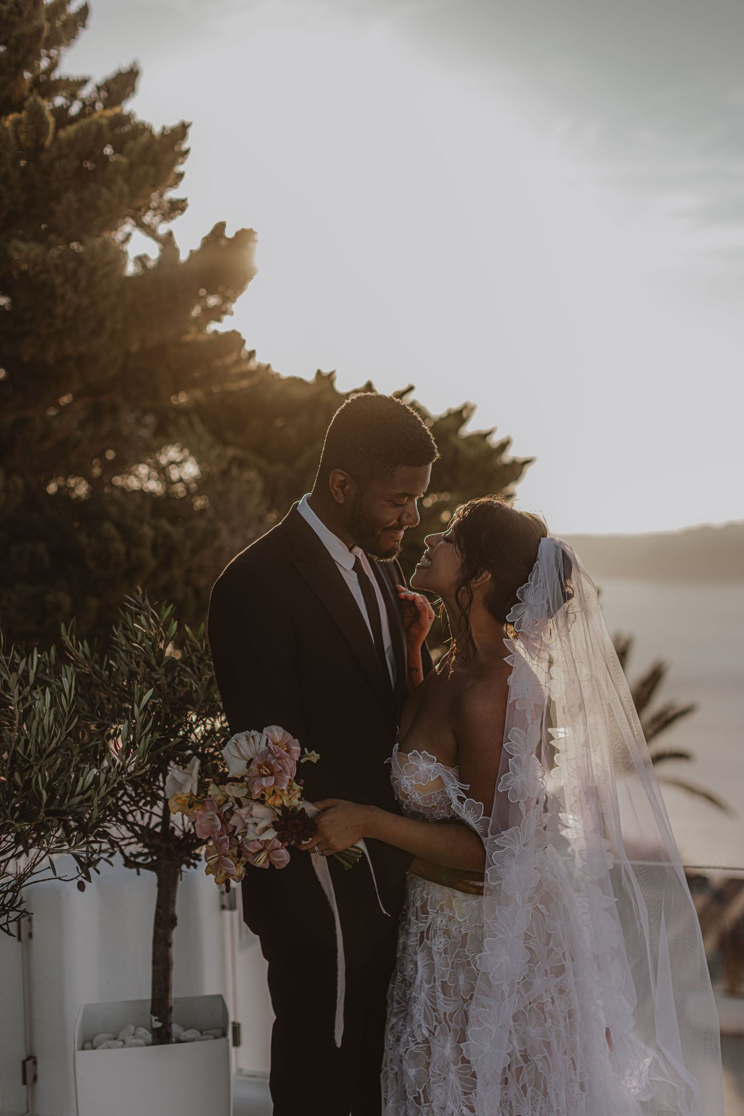 Intimate wedding couple moment captured against a scenic coastal backdrop at sunset.