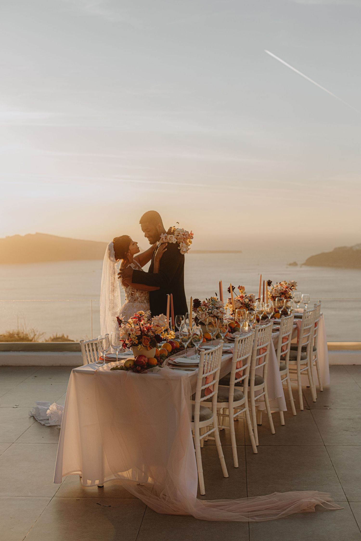 Romantic sunset wedding reception with white linens and floral centerpieces overlooking the ocean.