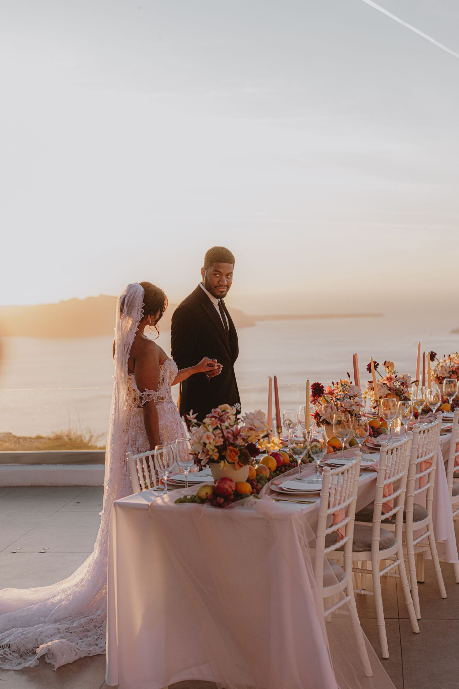Elegant wedding reception setup with white tables and chairs against a sunset oceanfront backdrop.