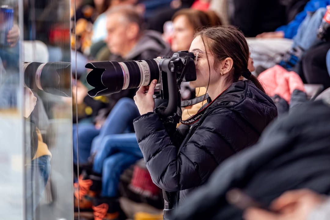 Sports photographer with telephoto lens capturing action from arena sidelines.