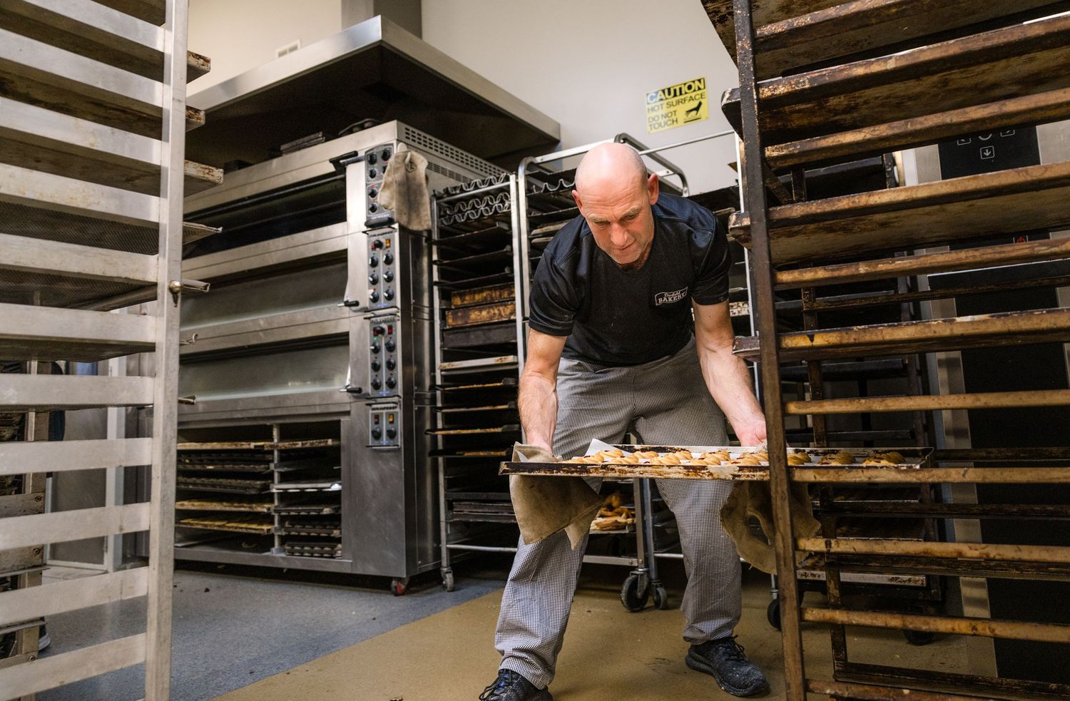 Artisan baker checking wooden proofing boards filled with fresh bread dough in a traditional bakery.