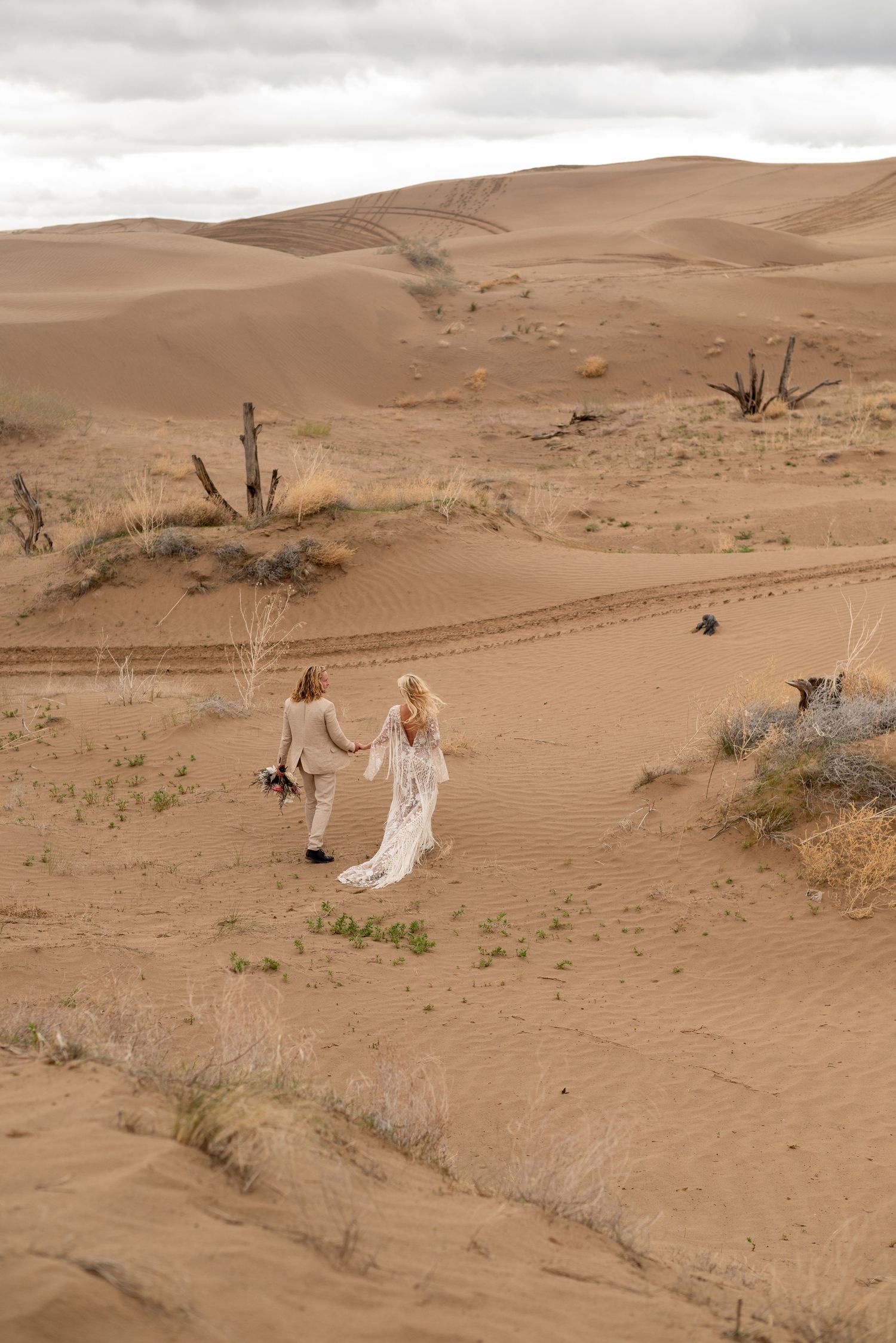 Wedding photography session in desert sand dunes with sparse vegetation.