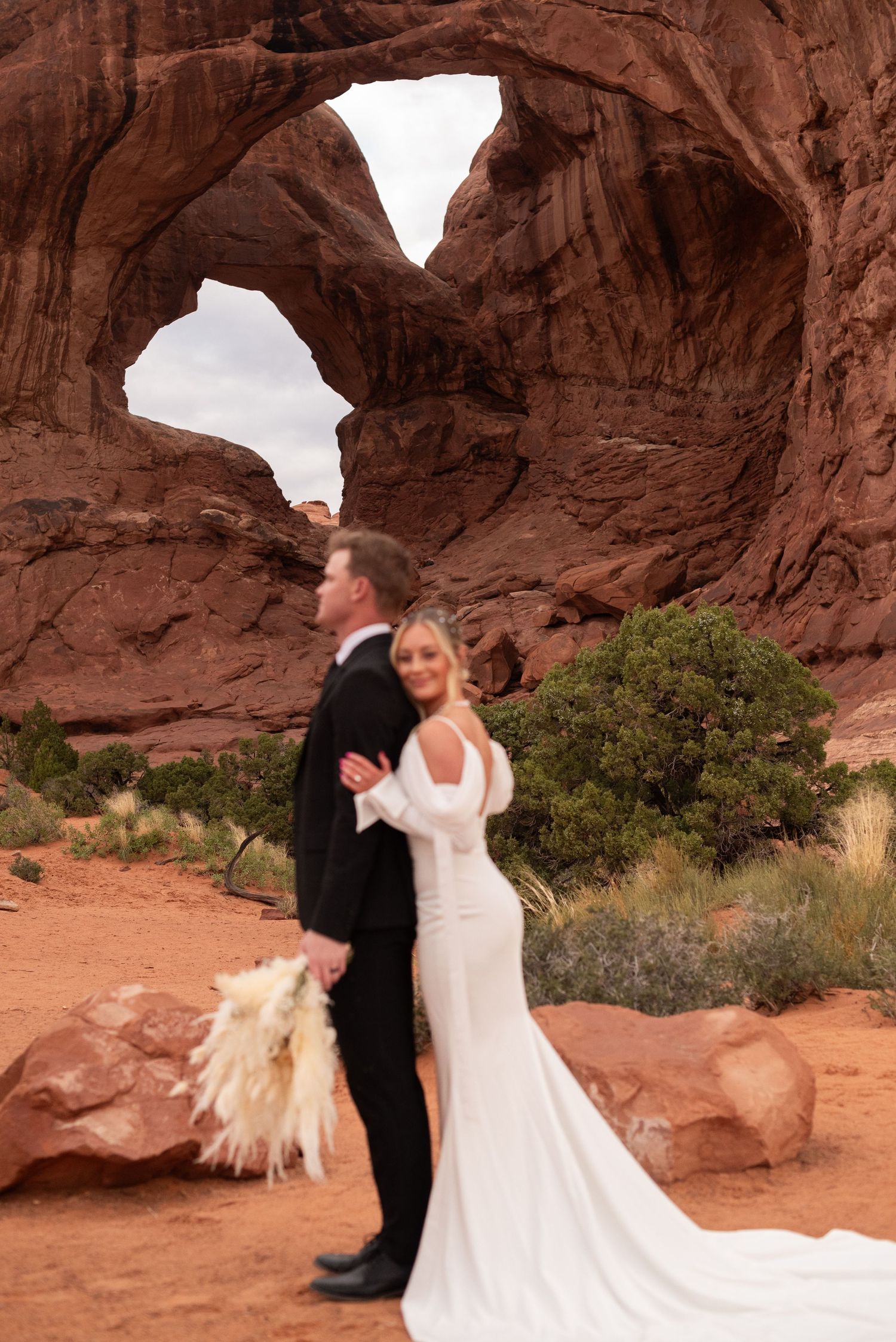 Wedding couple dances beneath massive red rock arches in desert landscape.