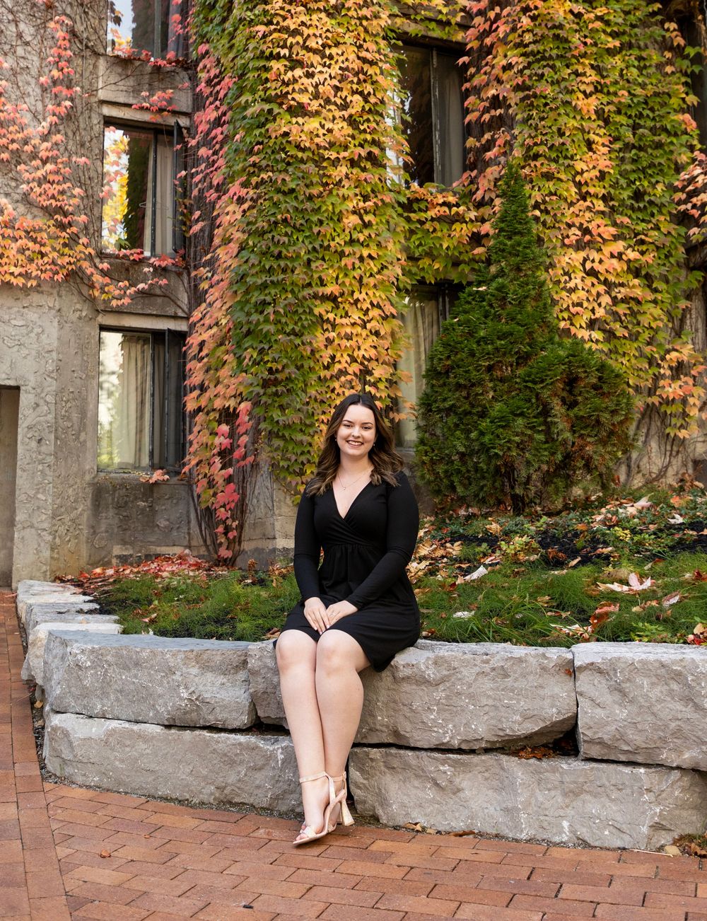 a female wearing a black dress sitting on rocks with her legs crossed