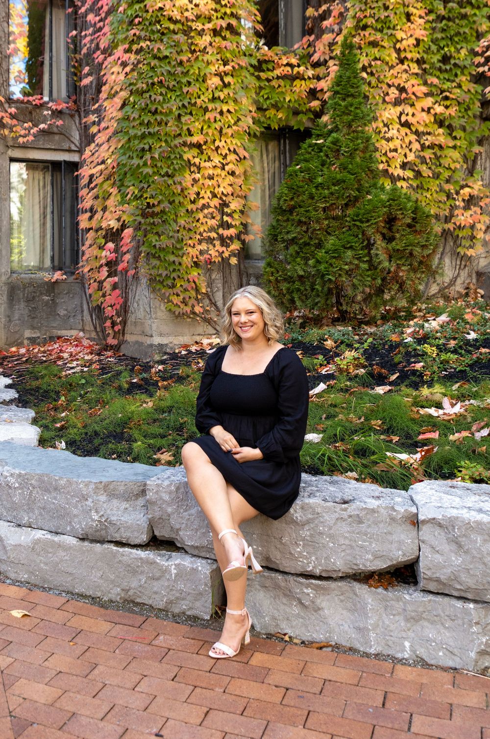 a female wearing a black dress sitting on rocks with her legs crossed