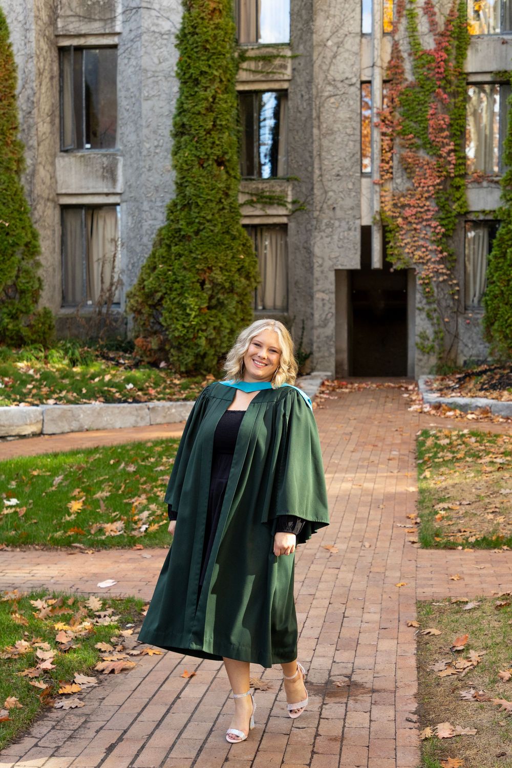 A female graduate walking through the trent champlain campus in the fall wearing her grad gown