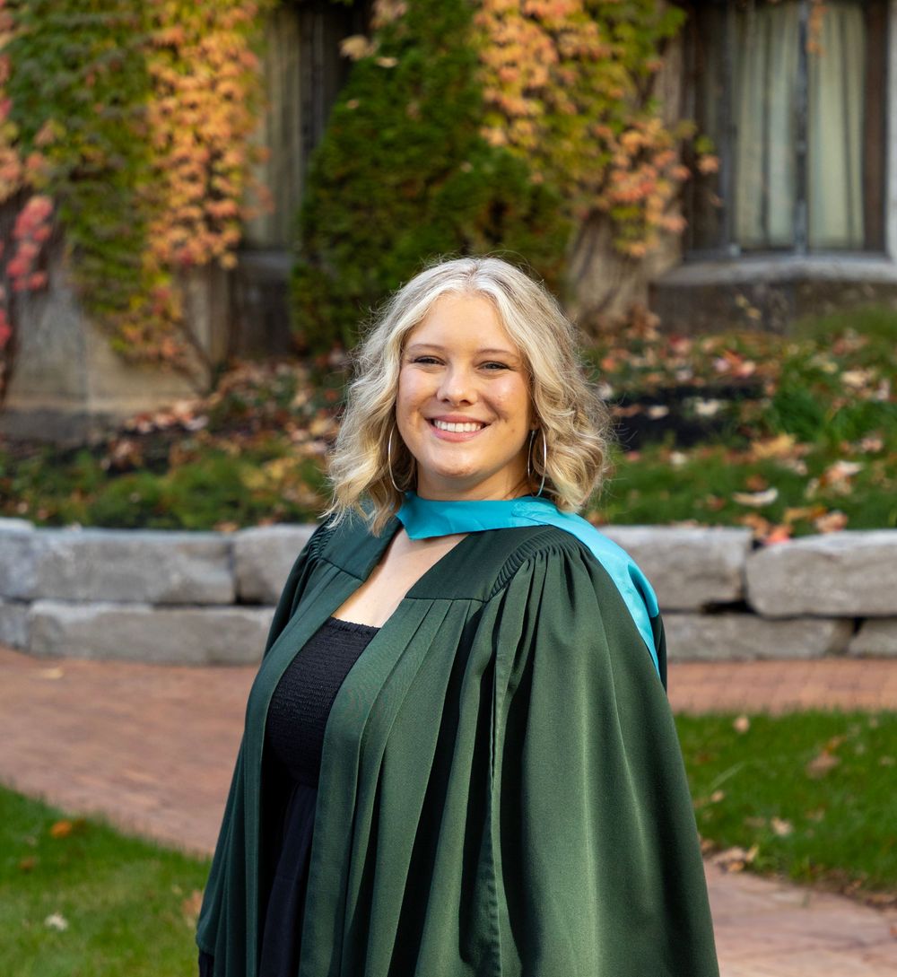 A close up of a female graduate in the fall wearing her grad gown