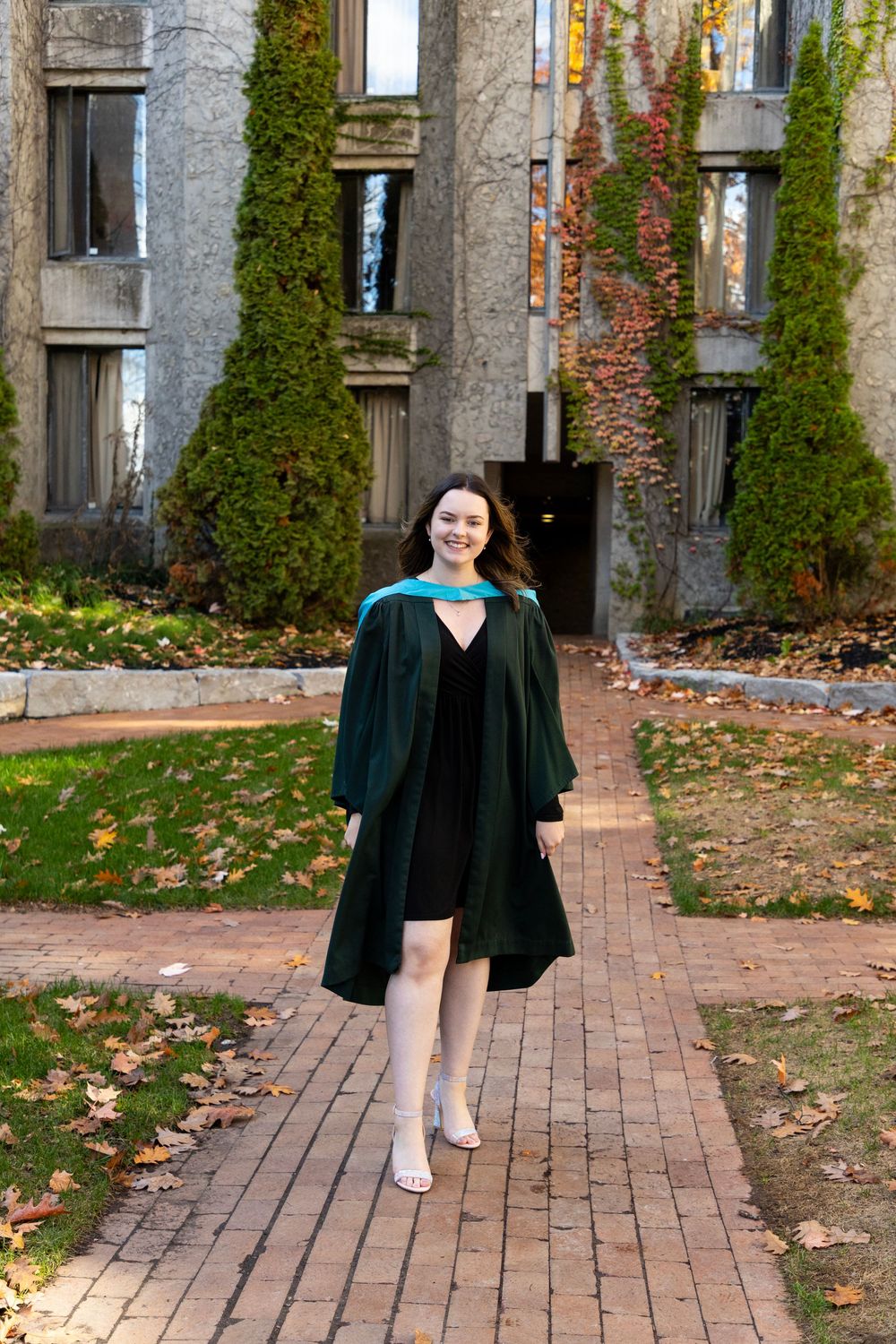 A female graduate walking through the trent champlain campus in the fall wearing her grad gown