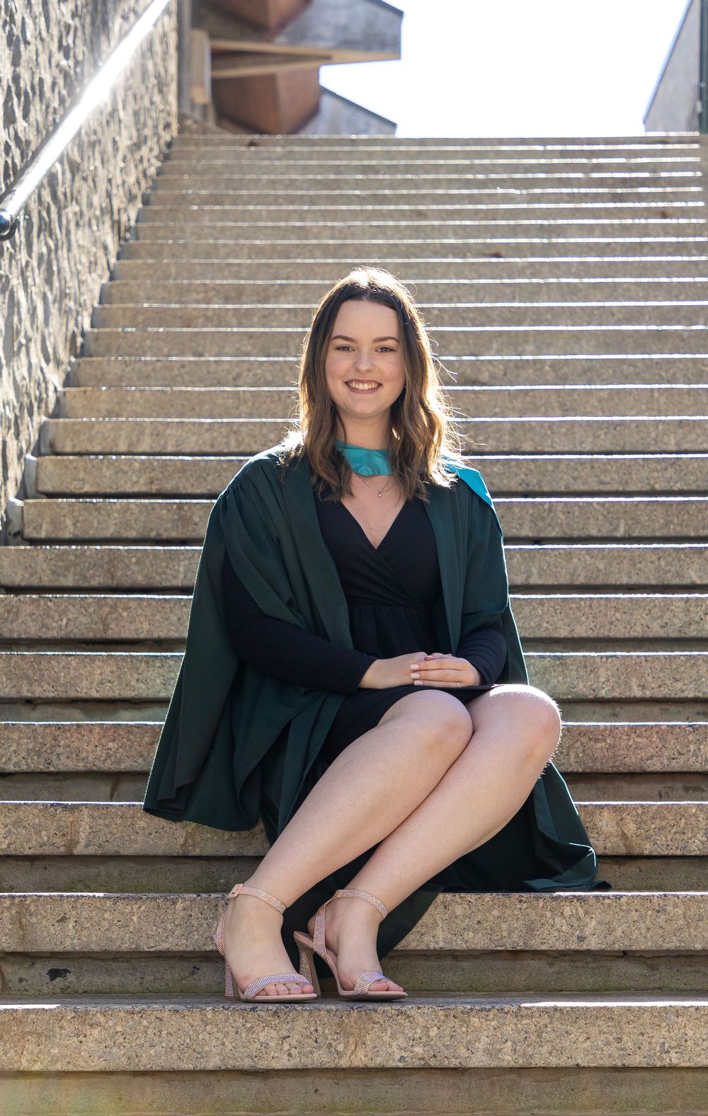 A female graduate of Trent University sitting on the campus stairs wearing her gown