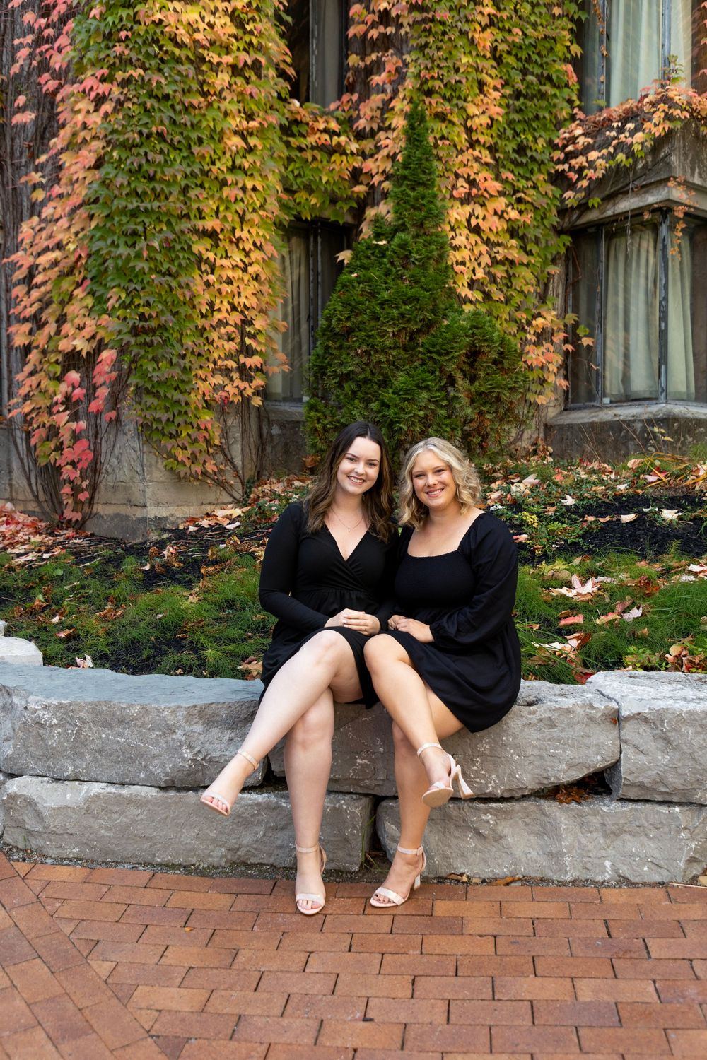 2 females wearing black dresses sitting on rocks with their legs crossed