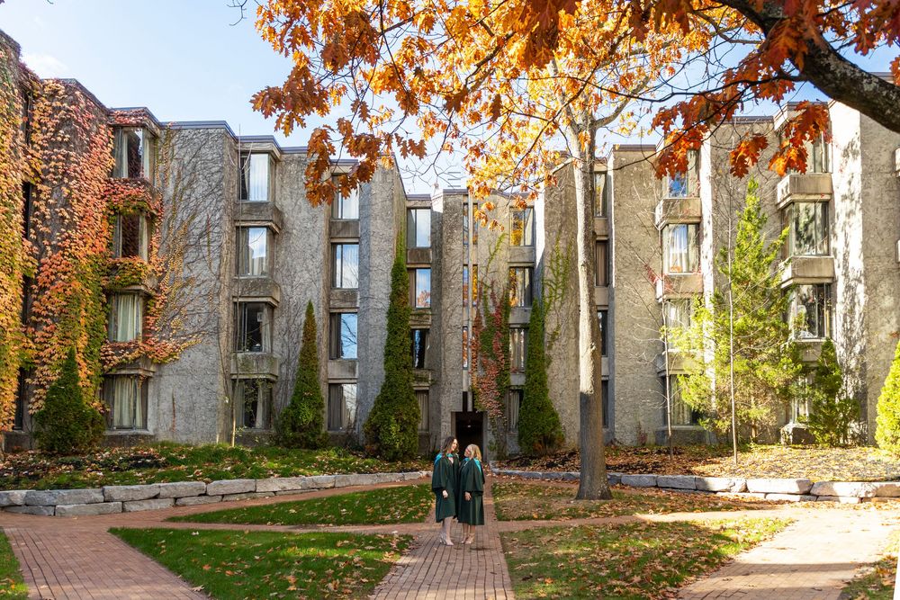 2 graduates looking at each other at the trent champlain campus in the fall wearing their grad gowns