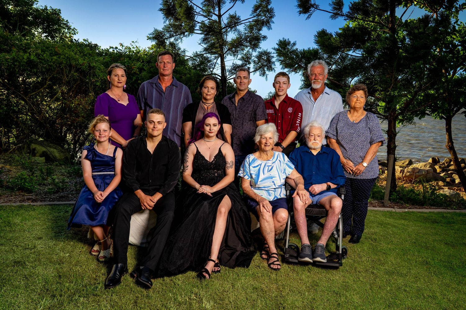 A group of people sit together on a grassy hillside for a casual outdoor family photo session.