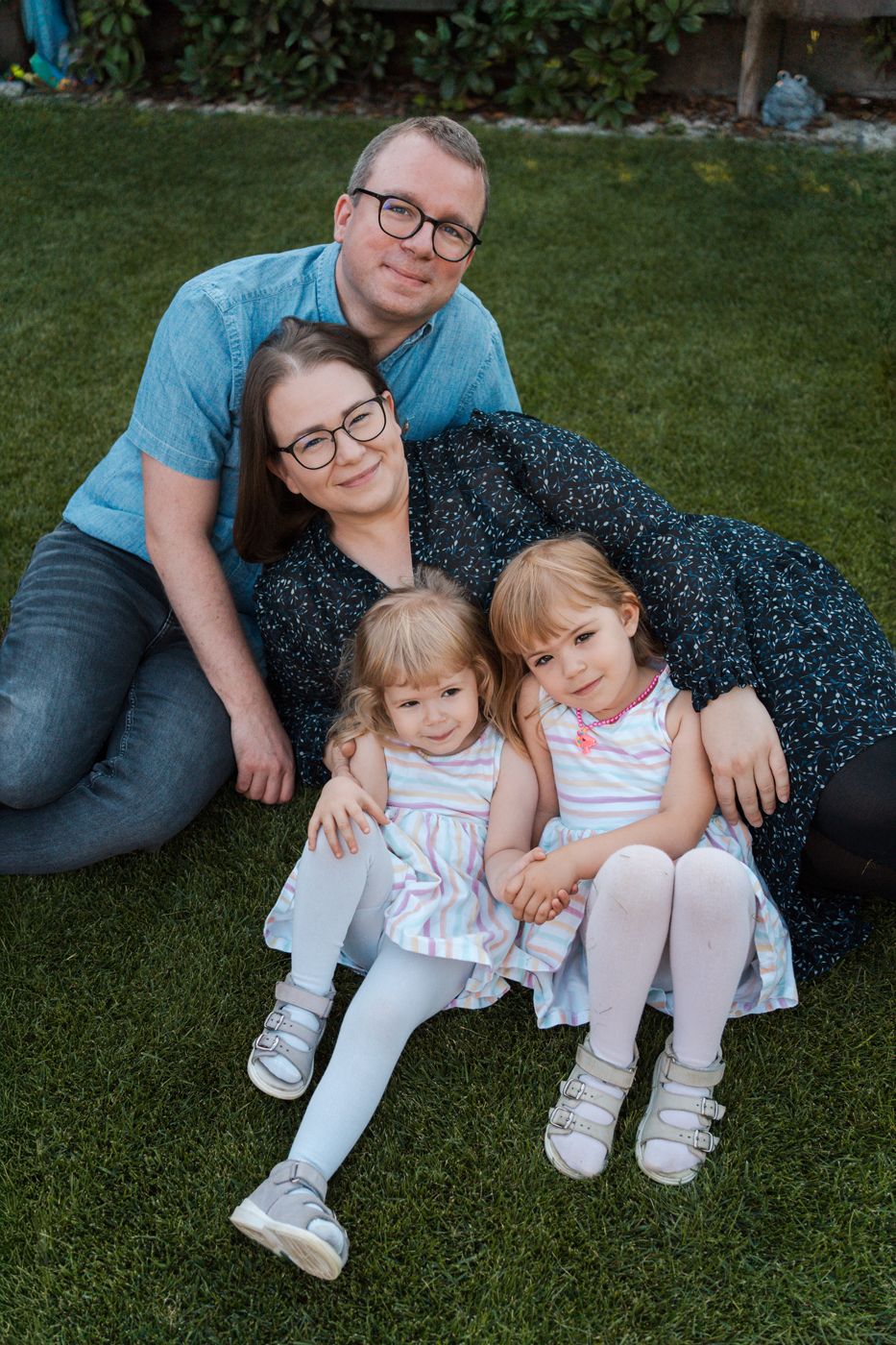 A family relaxes together on green grass in their backyard during a casual outdoor photo session in Rouse Hill