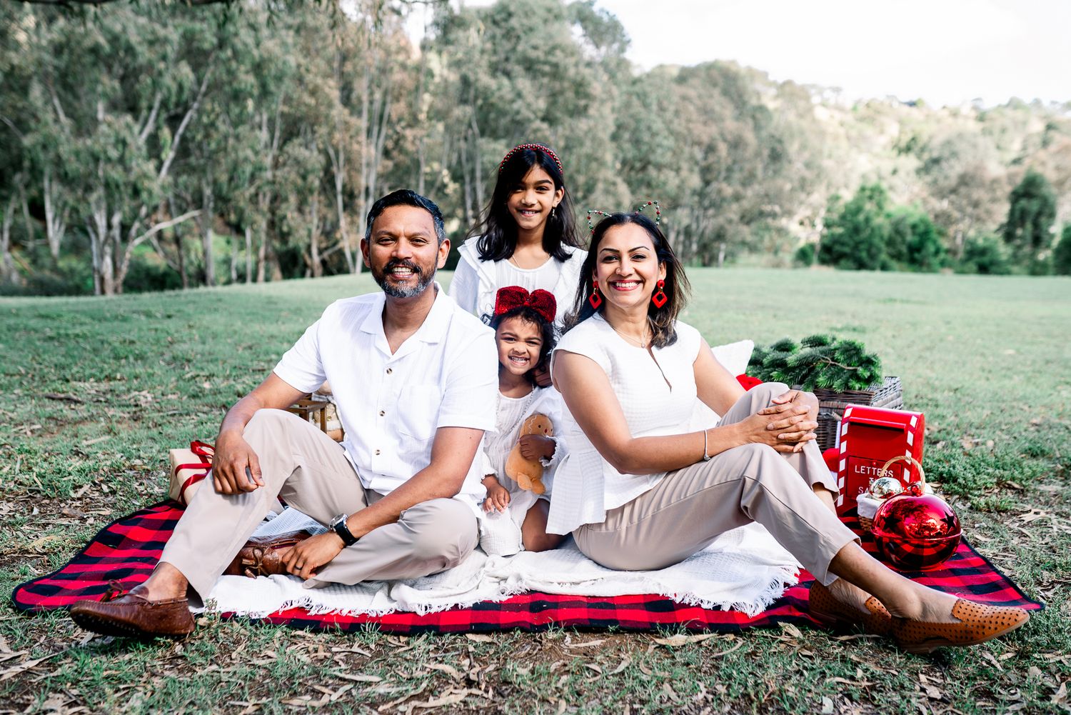 A family wearing white and khakis outfits sitting on a Christmas picnic setup during a Melbourne Christmas mini session in a park.