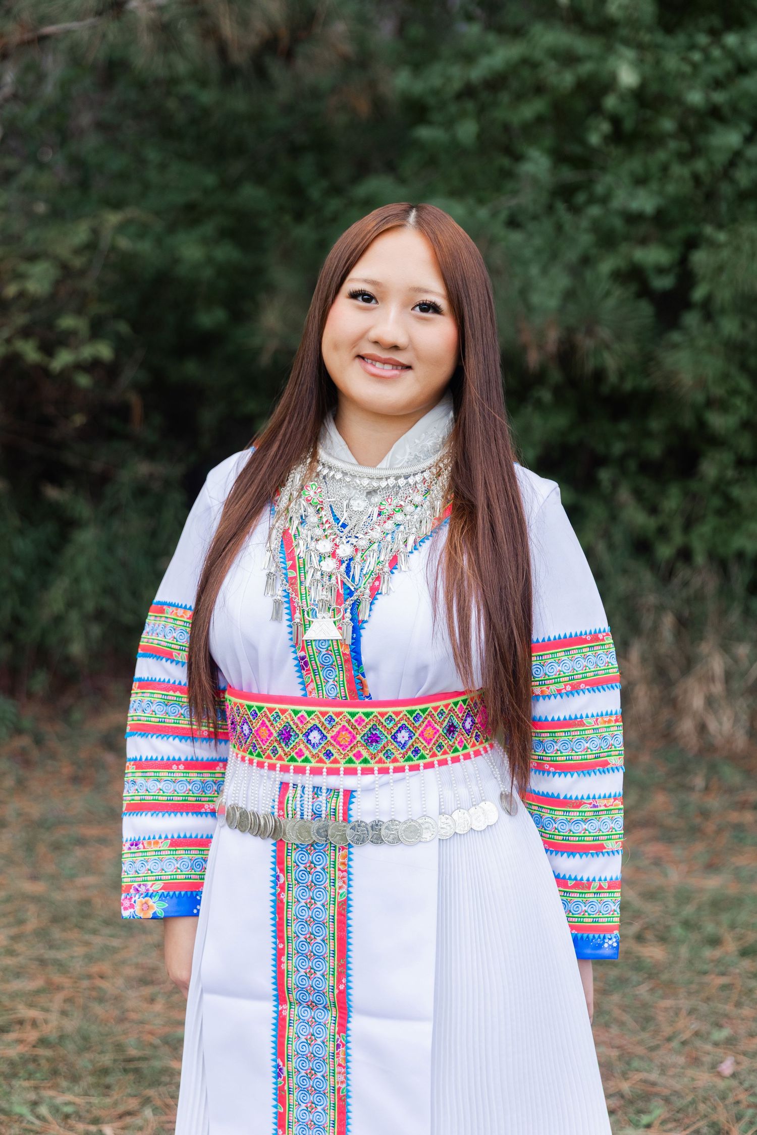 Woman wearing traditional white dress with colorful embroidered details in outdoor setting.