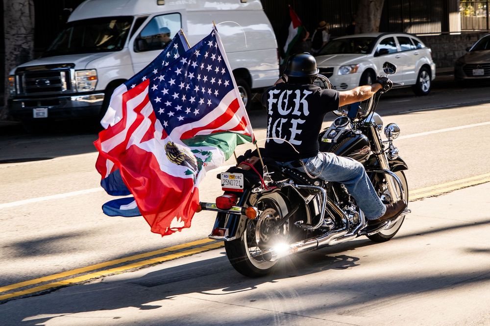 A motorcycle with flags and a "FUCK ICE" t-shirt drives by the “No Kings” protest in Los Angeles, California in October 2025.