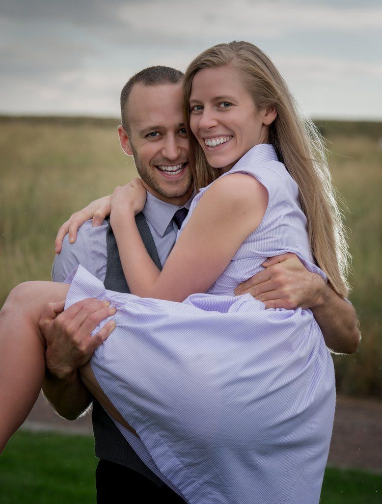 A happy couple embraces in a romantic pose against a rural landscape during an outdoor photoshoot.