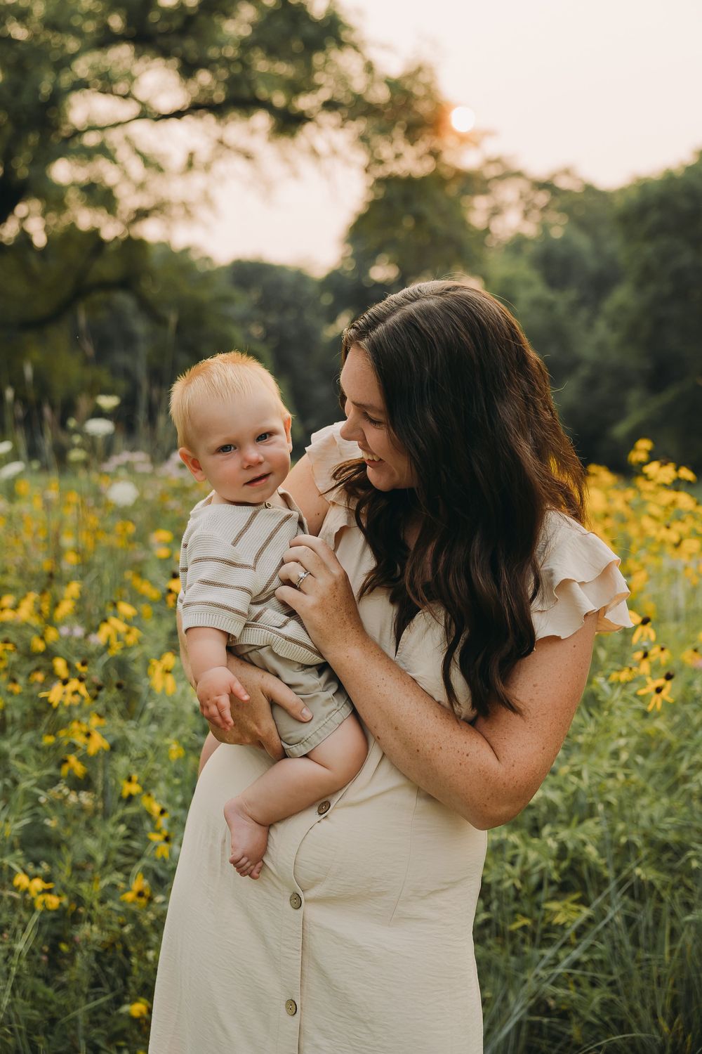 Mother and baby share tender moments together in a golden wildflower field during sunset.
