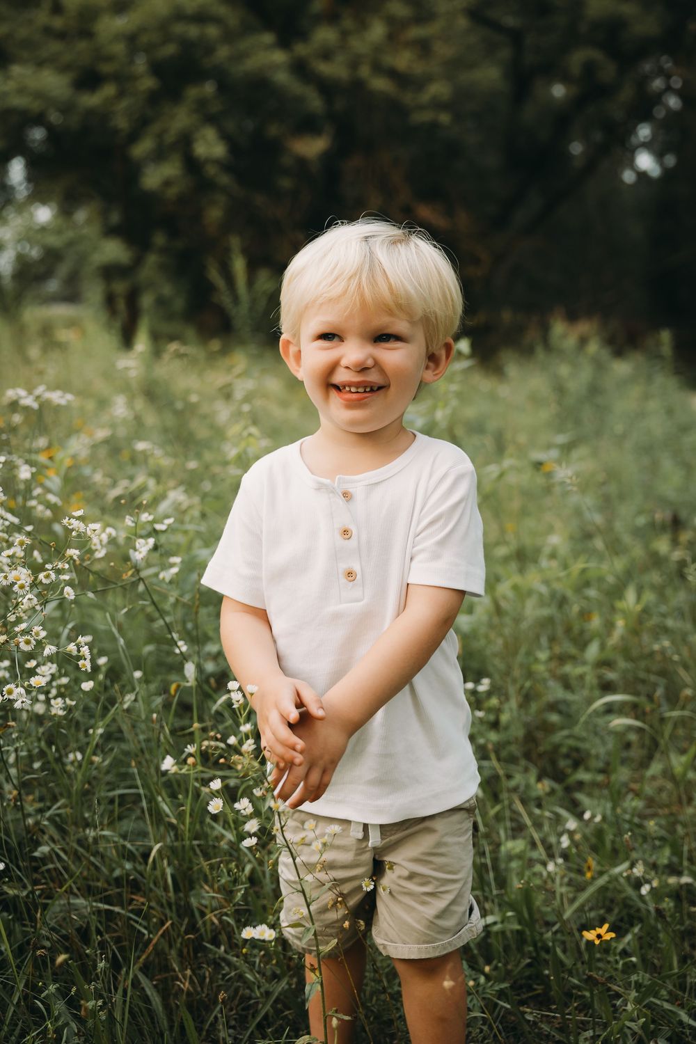 A young child in white shirt and khaki shorts plays in a wildflower meadow on a summer day.